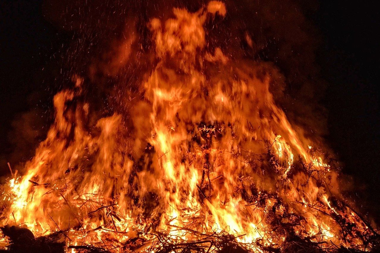 Ein Lagerfeuer brennt in der Nacht, seine Flammen reichen hoch in den dunklen Himmel und beleuchten die Umgebung.