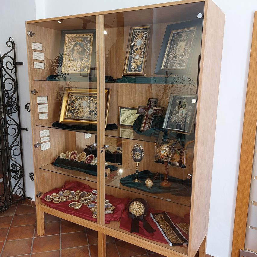 A wooden display cabinet with glass doors showcases various ornate frames and decorative items. The shelves are filled with framed pictures, decorative eggs, and other small objects.