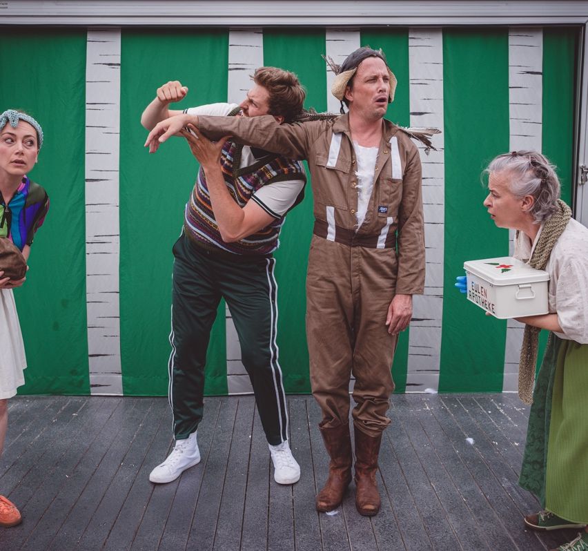 Four people on a stage, two men and two women, one holding a box, another with a feather headdress.