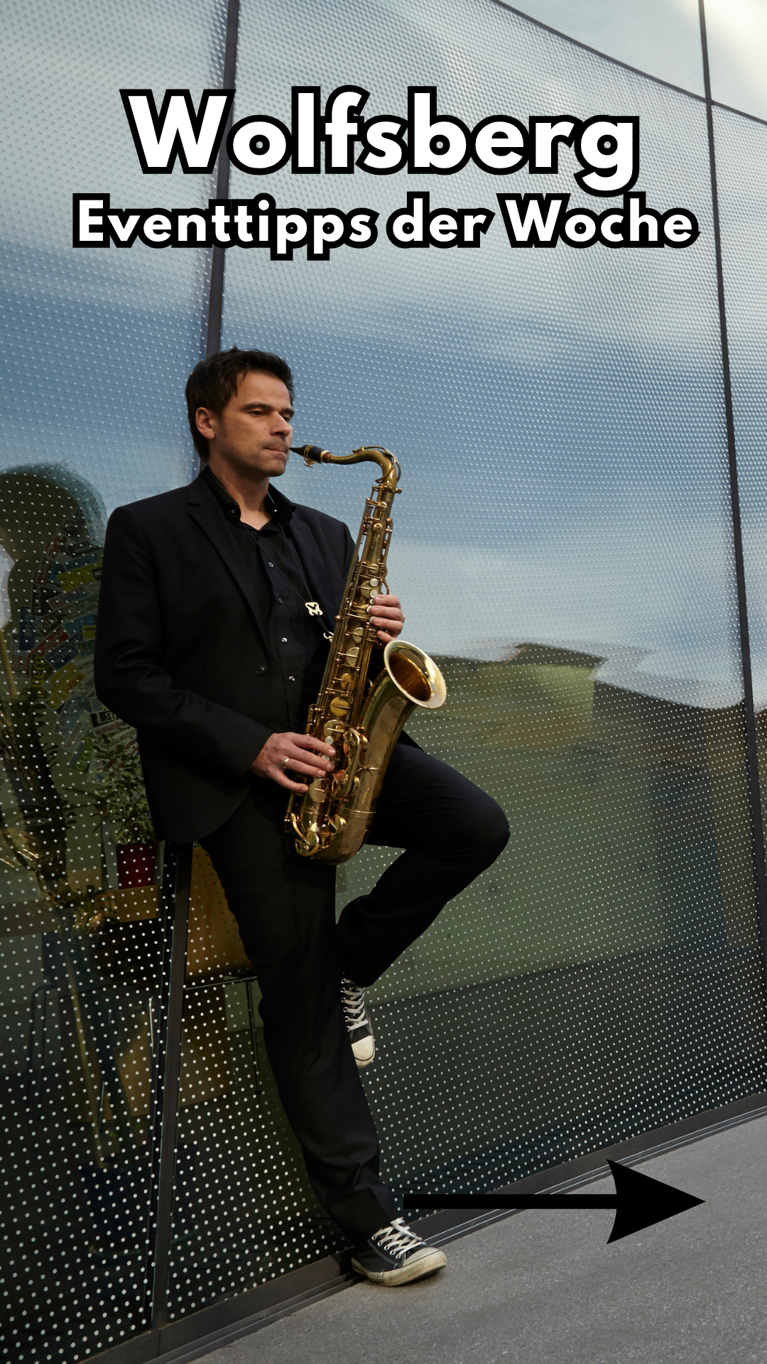 A man dressed in black holds a saxophone in front of a glass wall with a reflective surface.