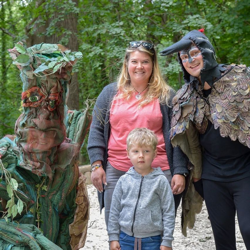 Eine Familie posiert mit zwei Personen in aufwendigen Kostümen, eine wie ein Baum, in einer Waldumgebung.