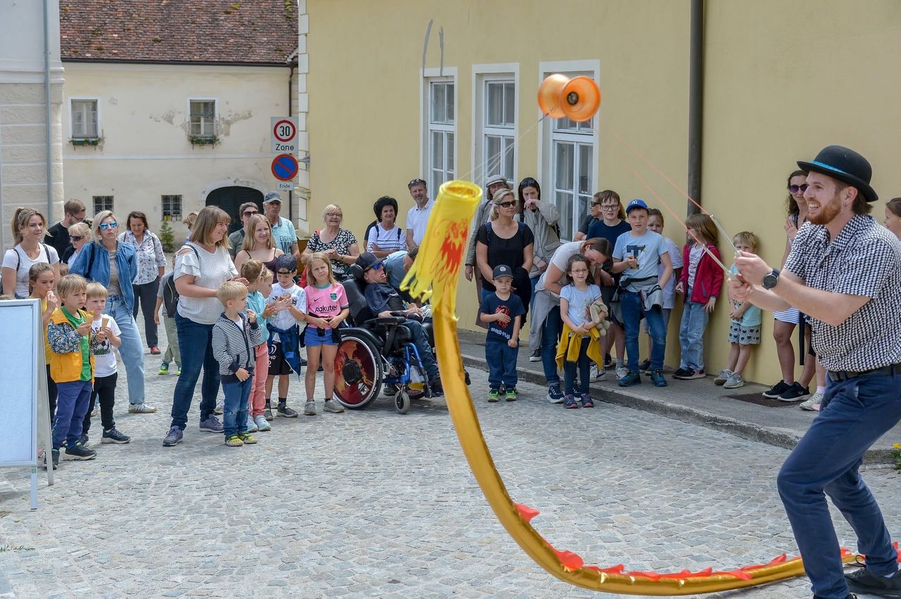 Eine Menschenmenge aus Erwachsenen und Kindern, die eine Straßenaufführung mit einem großen gelben Drachen auf einer Kopfsteinpflasterstraße beobachtet.