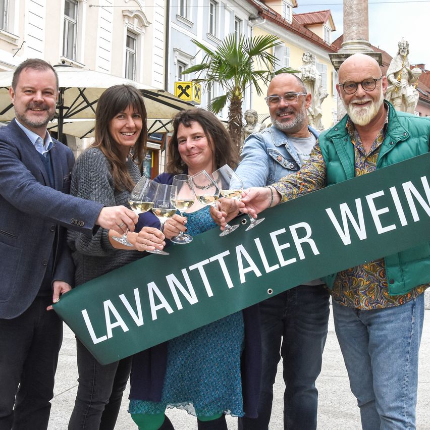 Fünf Personen halten Weinglas und ein grünes Schild mit Lavanttaler Wein vor einem Gebäude.