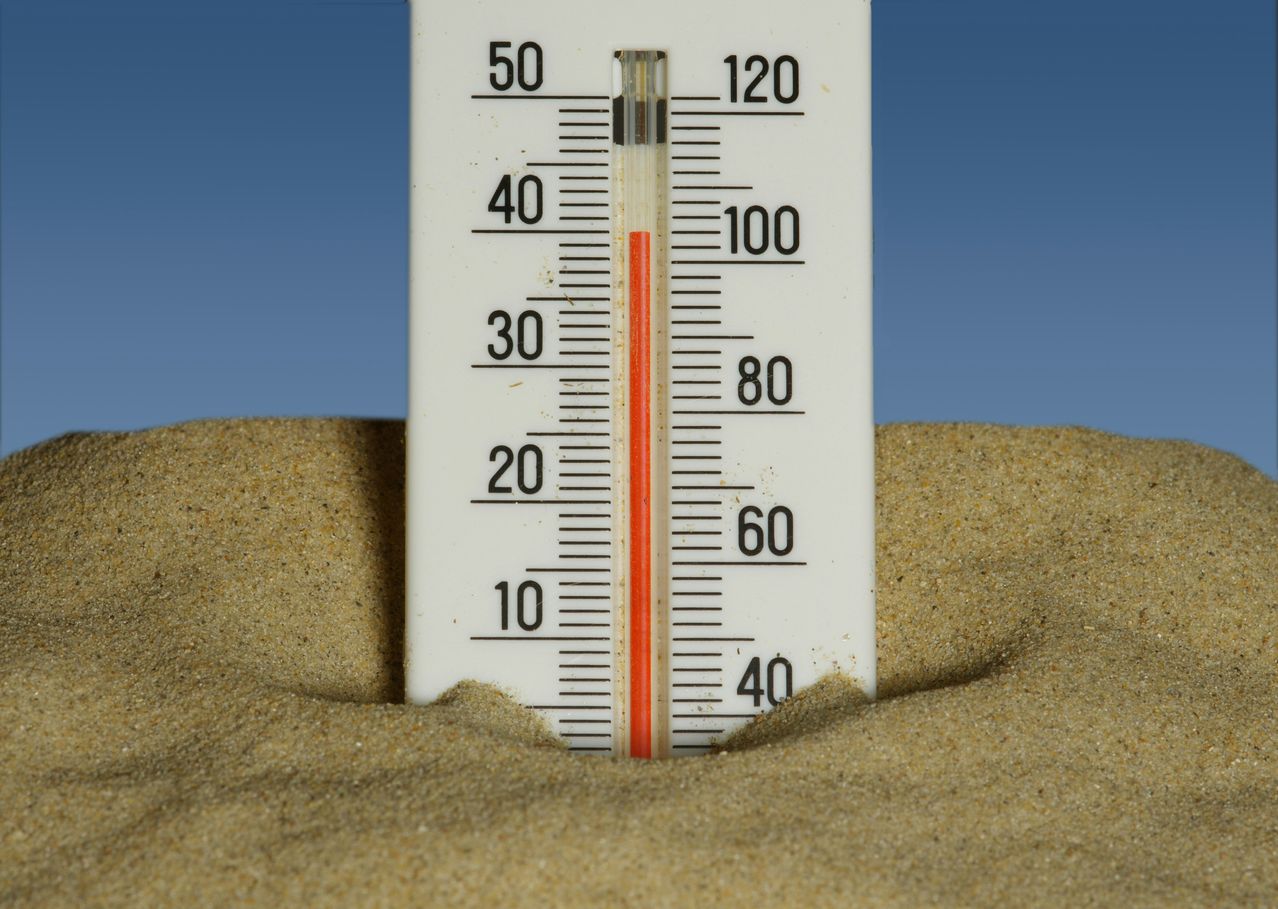 Ein Thermometer, das an einem sonnigen Tag im Sand vergraben ist. Die Temperaturen reichen von 10 bis 120.