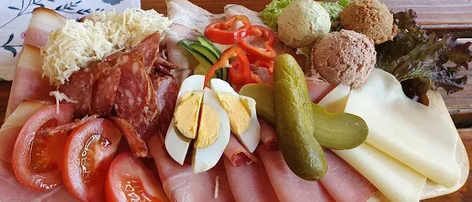 Ein Holztisch hält eine große Platte mit verschiedenen Fleischsorten, Käse und Gemüse. Es enthält Schinkenscheiben, eine Gurke, Tomaten und Eier.