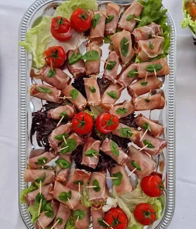 Ein silbernes Tablett hält eine Auswahl an Fleischspießen, die jeweils in Basilikumblätter gewickelt und mit Kirschtomaten auf Stöcken garniert sind. Die Spieße sind auf einem Bett aus Salatblättern angeordnet.