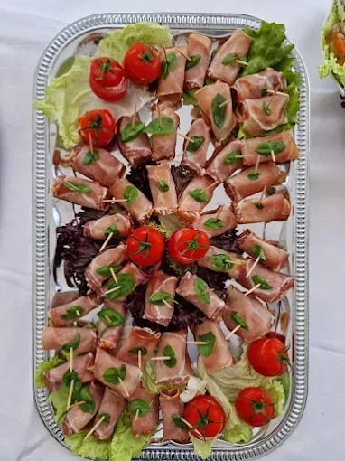 Ein silbernes Tablett hält eine Auswahl an Fleischspießen, die jeweils in Basilikumblätter gewickelt und mit Kirschtomaten auf Stöcken garniert sind. Die Spieße sind auf einem Bett aus Salatblättern angeordnet.