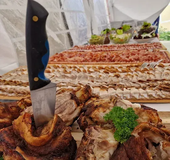 Ein Tisch mit verschiedenen Fleischsorten, darunter Scheiben von gepökeltem Fleisch, gebratenen Fleischstücken und einem Messer mit blauem Griff auf einem Knochen.