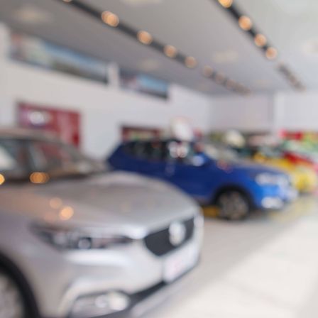 Ein verschwommenes Bild eines Autohauses mit einigen Autos, die in einer Reihe geparkt sind. Die Autos sind in verschiedenen Farben.