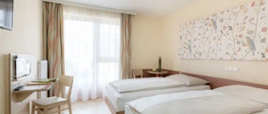 Ein Hotelzimmer mit zwei Betten, einem Schreibtisch, einem Stuhl und einem Fenster mit Vorhängen. An der Wand befindet sich ein Flachbild-TV.