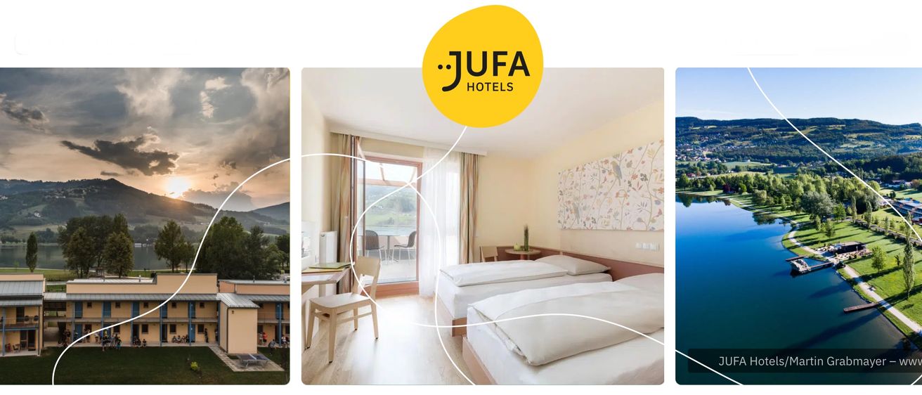 Ein Jufa-Hotelzimmer mit zwei Betten und einem Schreibtisch mit einem Stuhl vor einer Glastür, die zu einem Balkon führt.