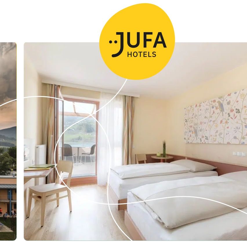 Ein Jufa-Hotelzimmer mit zwei Betten und einem Schreibtisch mit einem Stuhl vor einer Glastür, die zu einem Balkon führt.