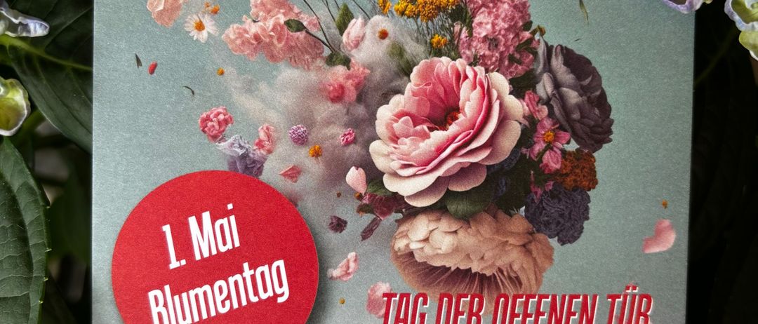 Plakat mit Blumendesign, Text 'Tag der offenen Tür' und Datum '1. Mai 2026', umgeben von Blumen. Ein roter Aufkleber lautet '1. Mai Blumentag'. Zeiten sind 9-12 und 13-16.