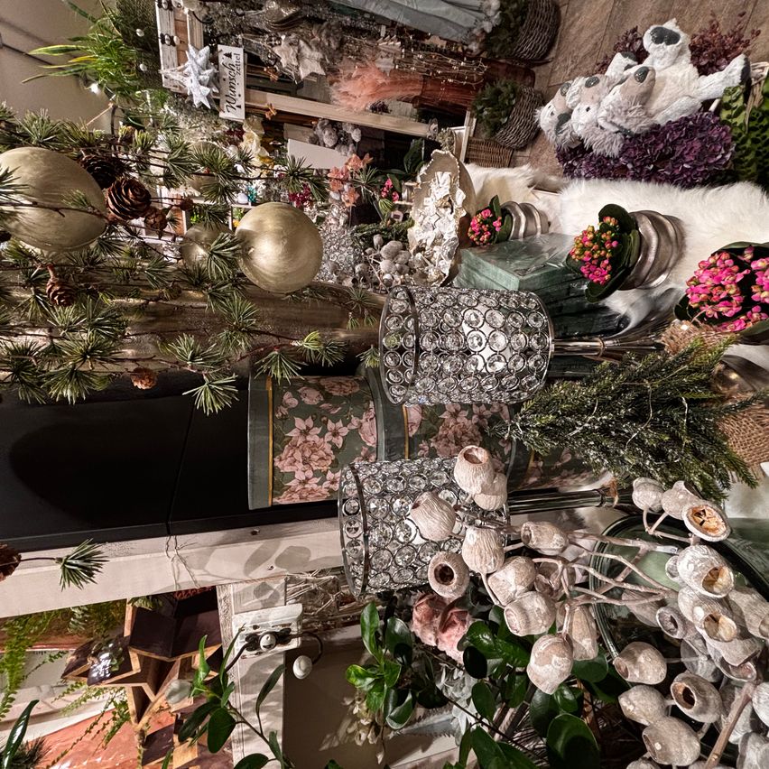 Ein Blick von oben auf einen dekorierten Laden mit verschiedenen Artikeln wie weißen und rosa Blumen, goldenen Ornamenten und Plüschtieren. Der Laden hat ein weißes Regal und einen schwarzen Rand.