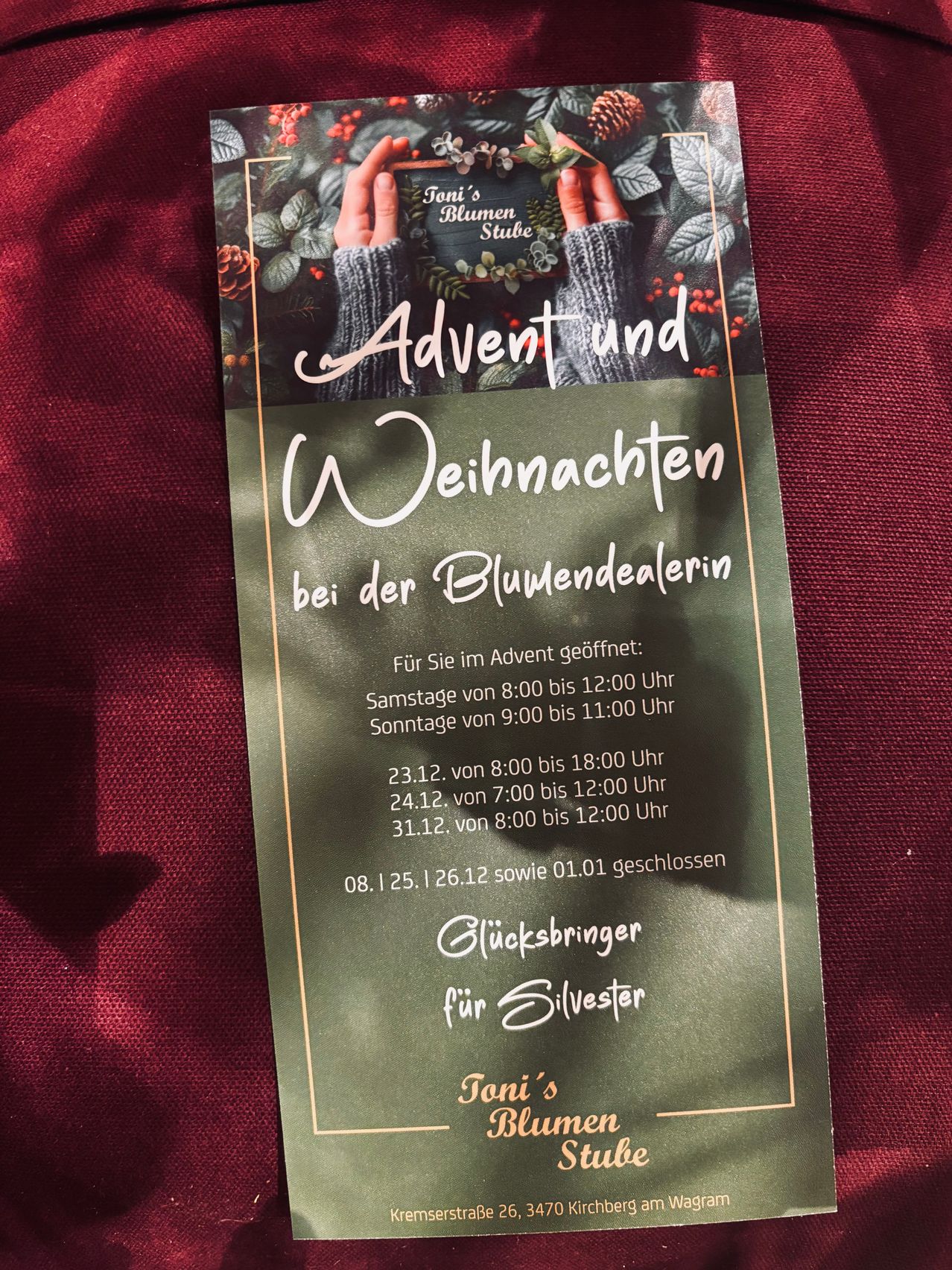 Ein Plakat für Advent und Weihnachten in einem Blumenladen. Öffnungszeiten sind aufgeführt, zusammen mit den Schließungdaten. Das Plakat zeigt einen festlichen Kranz und Hände, die ein Schild halten.