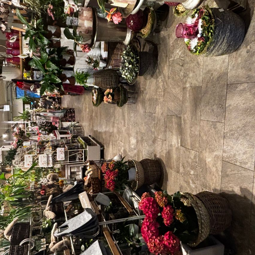 Ein Blick von oben auf ein Blumengeschäft voller verschiedener Pflanzen und Blumenarrangements. Körbe mit Blumen und Pflanzen sind an der Wand angeordnet. Einige sind auf dem Boden ausgestellt.