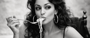 Eine Frau in einem schwarzen Kleid isst Spaghetti mit einer Gabel. Das Foto ist schwarz-weiß.