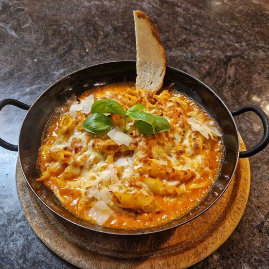 Eine Schüssel mit Käse und Basilikum auf einem Holzteller mit einem Stück Brot auf der Seite.