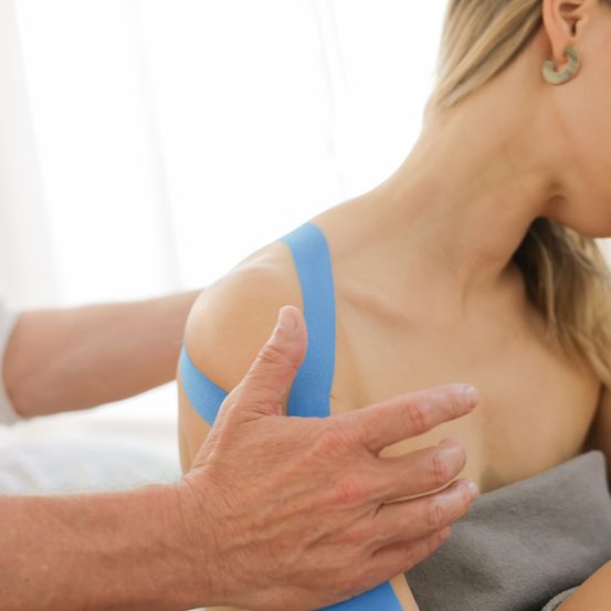 Eine Frau mit blauem Klebeband auf der Schulter wird von einem Mann massiert.