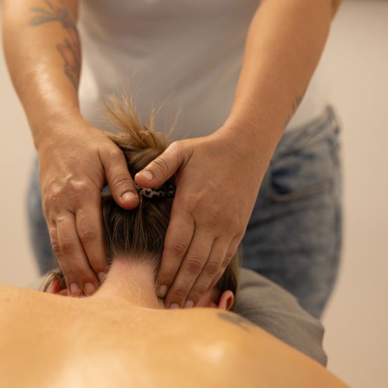 Eine Person erhält von einer anderen Person eine Kopfmassage mit beiden Händen. Die Person, die die Massage erhält, schaut nach unten.