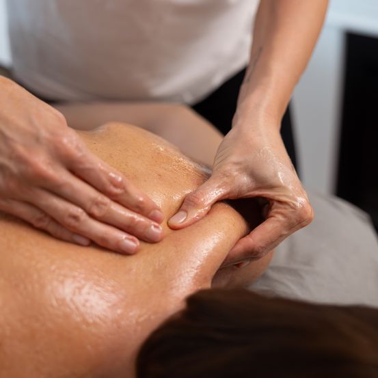Eine Person erhält eine Massage am Rücken und Schulterbereich, wobei die Hände des Therapeuten Druck ausüben.