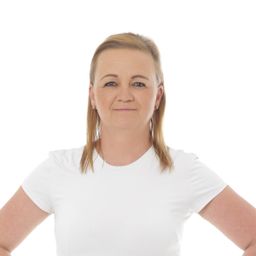 Eine Frau mit blonden Haaren, die ein weißes T-Shirt trägt, lächelt und posiert für ein Foto.