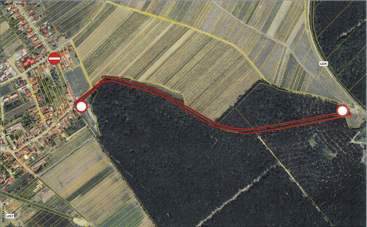 Eine Luftaufnahme einer Landschaft mit landwirtschaftlichen Feldern und Wäldern. Rote Linien markieren die Grenzen eines bestimmten Gebiets. Ein weißer Kreis hebt einen bestimmten Punkt hervor.