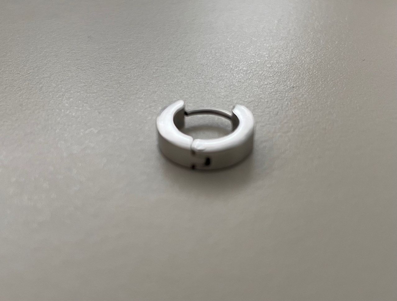 Ein silberner Ring liegt auf einer grauen Oberfläche, leicht gebogen und poliert.