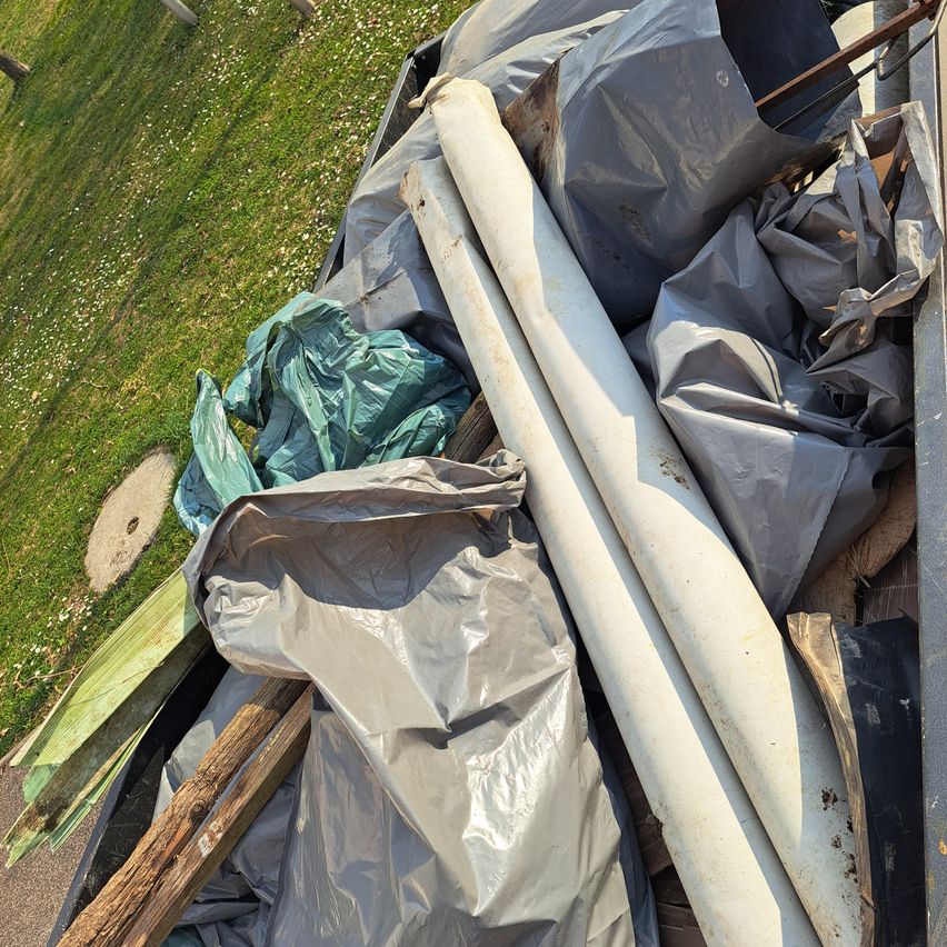 A collection of various debris including plastic bags, wooden planks, and metal pipes lies in a dumpster, scattered in a messy pile.