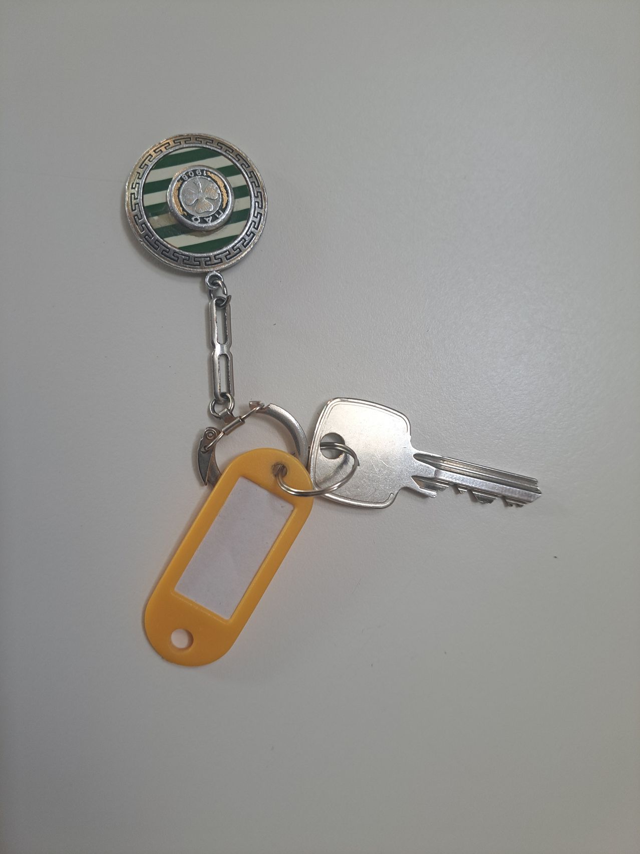 A keychain with a round charm and a yellow tag hangs on a silver key with a hole. The round charm has a green and white striped design.