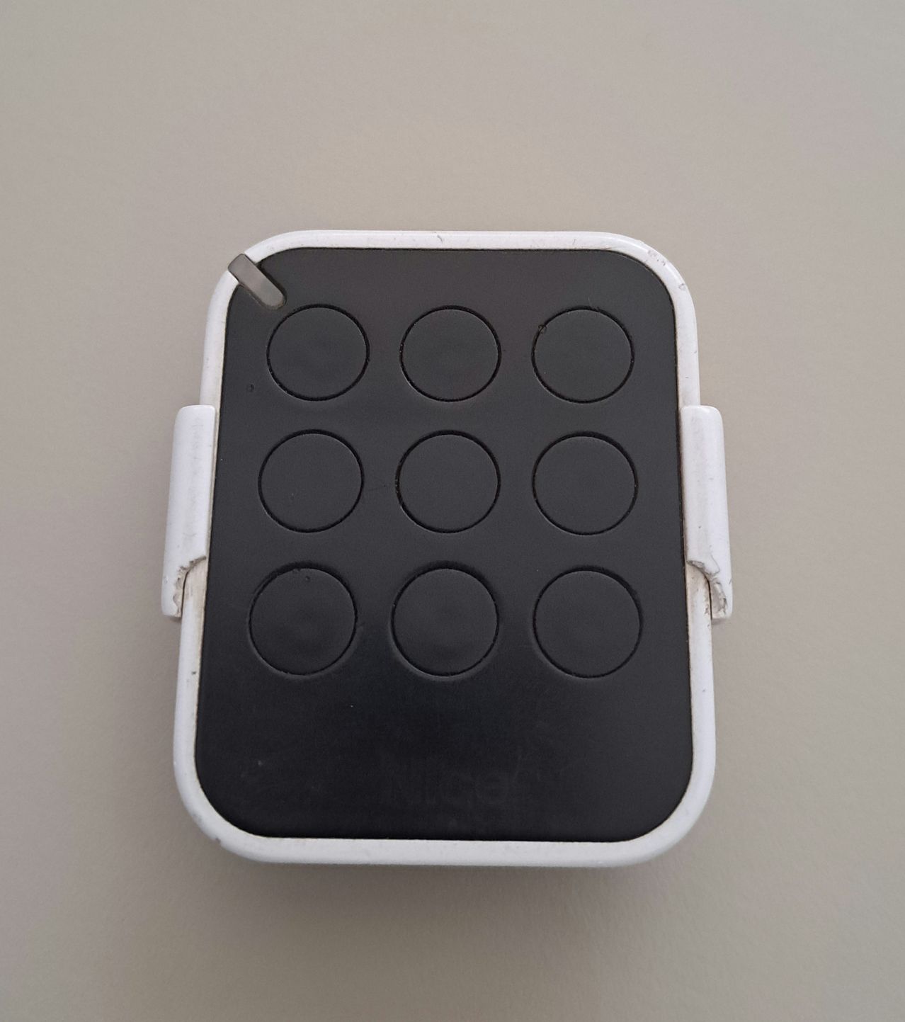 A square, black and white object with ten circular buttons arranged in a grid pattern. The object has a white border and appears to be a remote control or keypad.