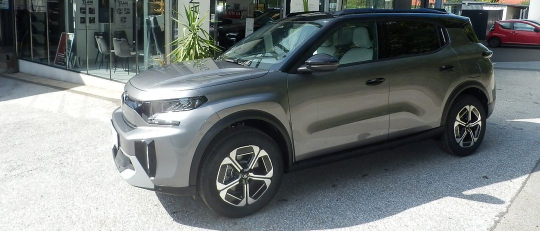 Ein grauer Citroen SUV steht vor einem Citroen-Händler mit einer Glasüberdachung.