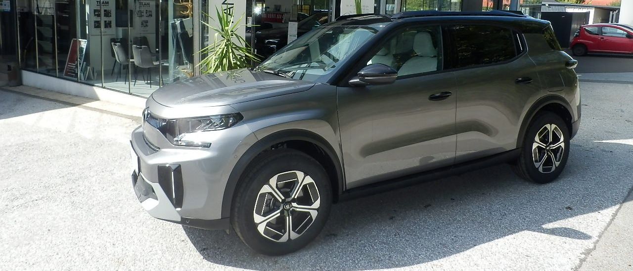 Ein grauer Citroen SUV steht vor einem Citroen-Händler mit einer Glasüberdachung.