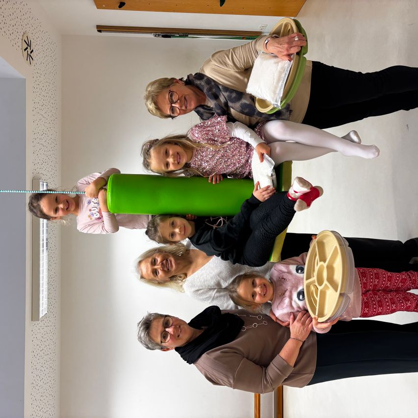 Eine Gruppe von Erwachsenen und Kindern steht in einem Raum. Sie lächeln und posieren für ein Foto. Einige von ihnen halten Teller und Schüsseln.