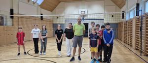 Eine Gruppe von Personen, darunter ein Mann, zwei Frauen und mehrere Kinder, stehen gemeinsam in einer Turnhalle und lächeln für ein Foto.