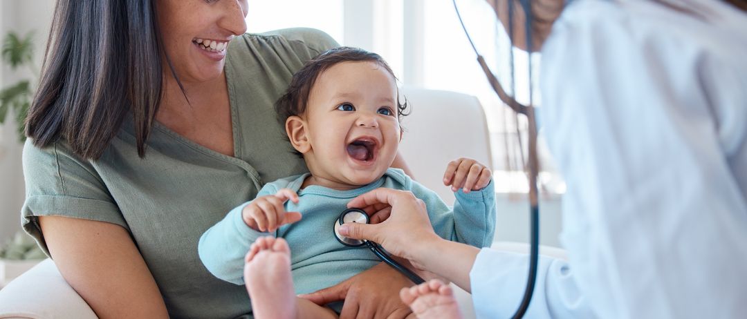 Eine Ärztin überprüft das Herz eines Babys mit einem Stethoskop, während das Baby lacht und die Mutter lächelt.