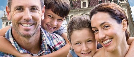 Eine vierköpfige Familie, zwei Erwachsene und zwei Kinder, lächelt und posiert für ein Foto vor einem historischen Gebäude mit einem Uhrturm.