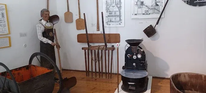 Ein Museumsdisplay mit alten Werkzeugen, einem Vintage-Holzrad, einer Statue eines Mannes in Latzhosen und einer großen schwarzen Maschine auf einem Holzboden.