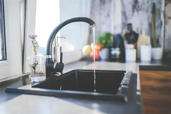 A sink with running water in a kitchen, a faucet, and a vase with a flower.