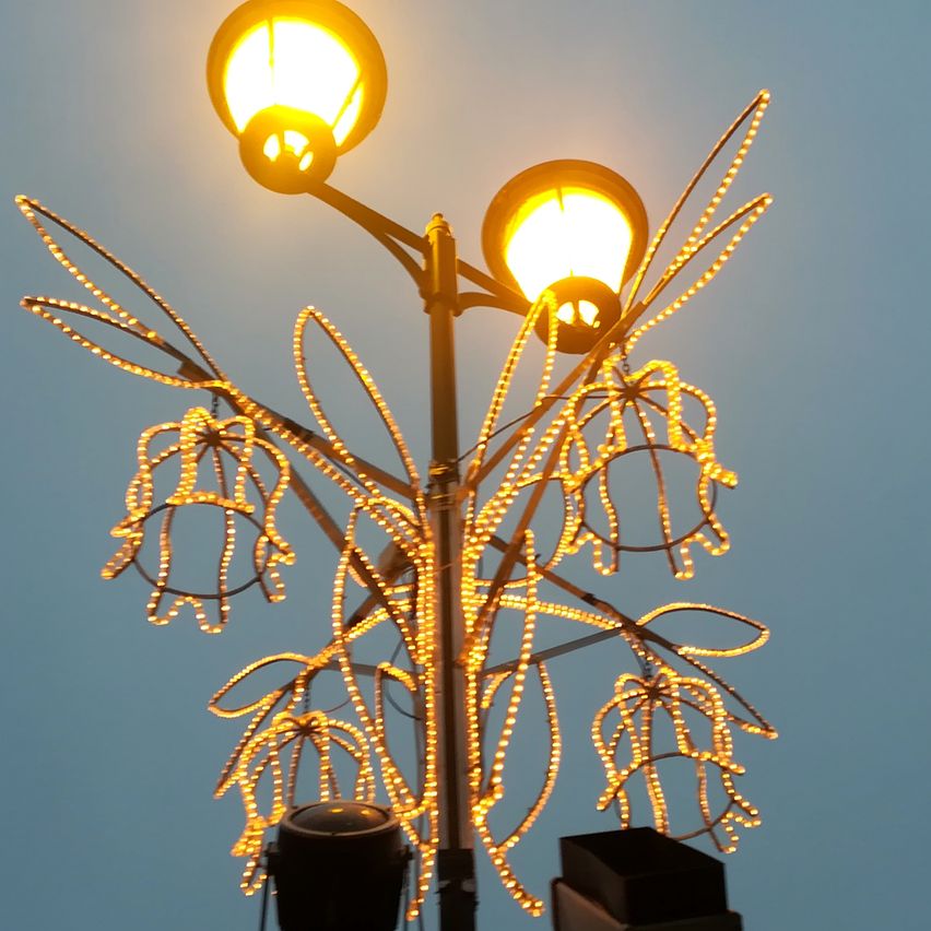 Eine Straßenlaterne mit dekorativen Lichtern in Form von Blumen hängt an ihren Zweigen und beleuchtet den Bereich mit einem warmen Schein in der Nacht.