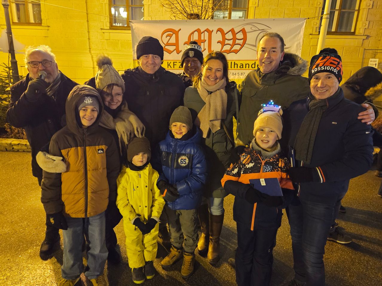 Eine Gruppe von Menschen, einschließlich Erwachsener und Kindern, steht gemeinsam für ein Foto vor einem Gebäude. Sie sind alle warm gekleidet, und einige von ihnen tragen Mützen.