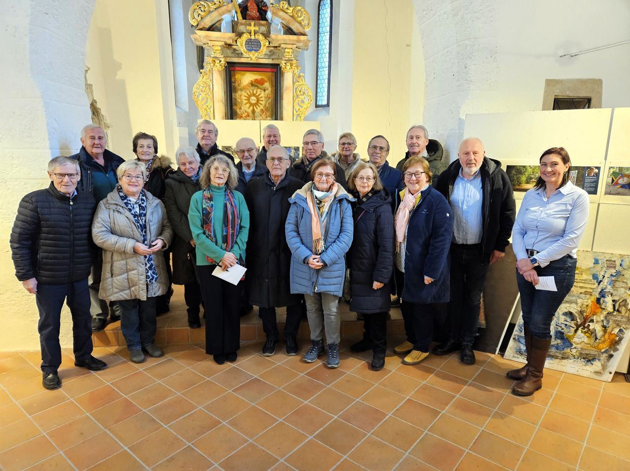 Eine Gruppe von Menschen in Wintermänteln und mit Brillen steht in einer Kirche und posiert für ein Foto vor einem Altar.