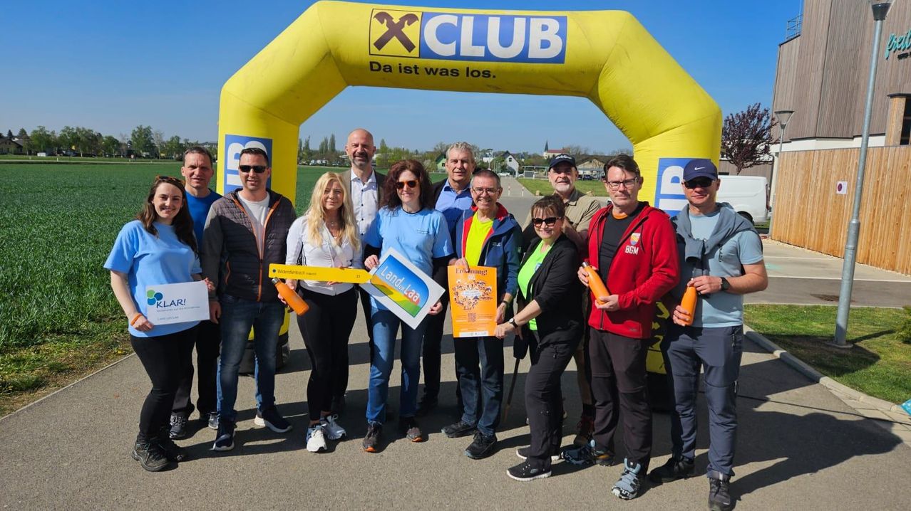 Eine Gruppe von Menschen, die zusammen mit gelben und orangefarbenen Bannern steht, eine Frau hält eine Karte, und sie posieren für ein Foto unter einem gelben Bogen mit den Worten X Club darauf.
