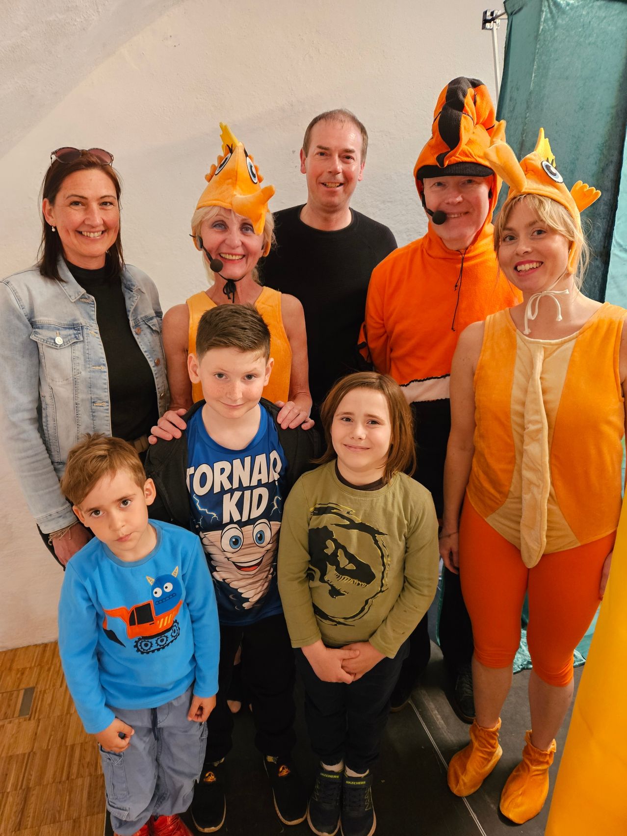 Eine Familie posiert für ein Foto mit drei Kindern vorne und drei Erwachsenen dahinter, alle in orange-gelben Kostümen.