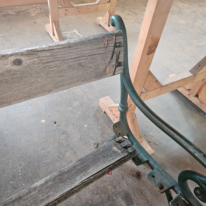 Eine Nahaufnahme einer Holzbank mit Metallhalterungen in einer Werkstatt. Die Bank zeigt sichtbare Abnutzungsspuren und ist an einer Holzstruktur befestigt.