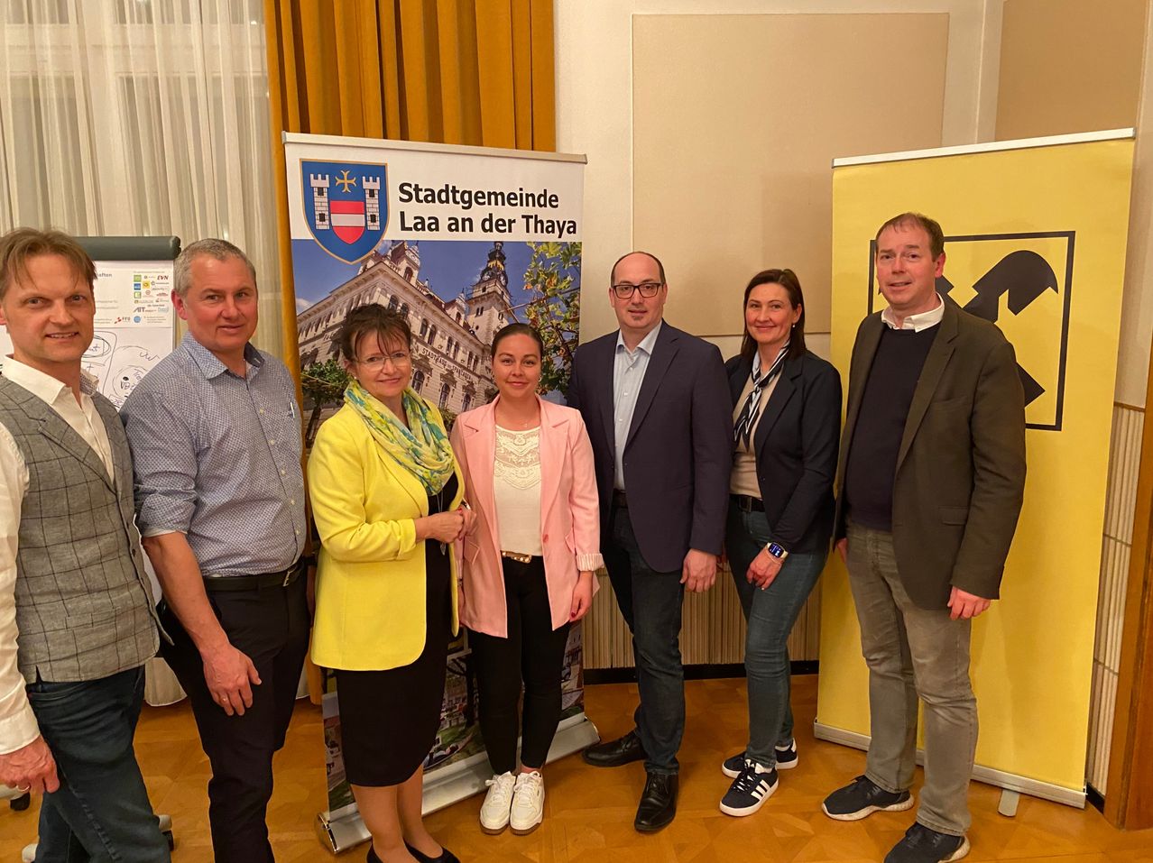 Fünf Menschen, wahrscheinlich Kollegen, stehen eng nebeneinander vor einem Werbebanner. Sie scheinen für ein Foto zu posieren.