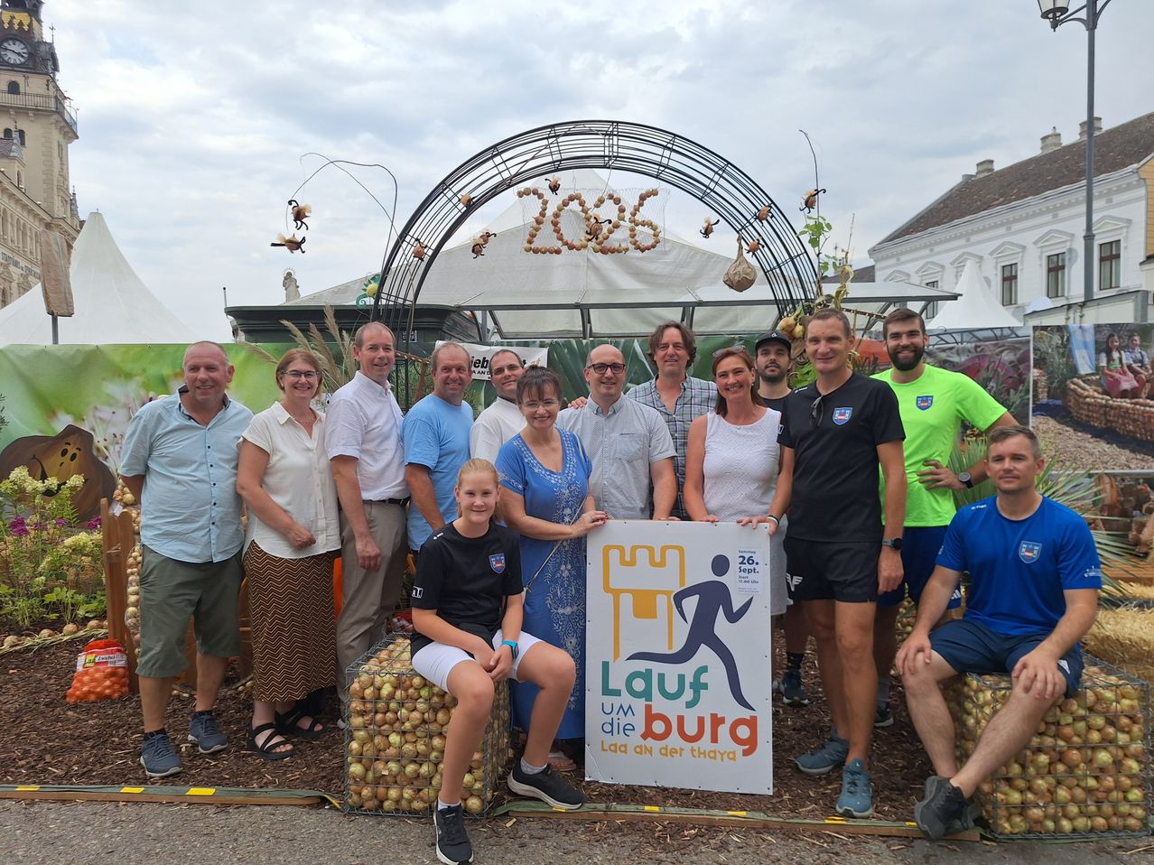 Eine Gruppe von Menschen posiert für ein Foto vor einem Schild, das Lauf um die Burg besagt. Sie stehen vor einem dekorativen Bogen mit einem Schild, das 2026 besagt.
