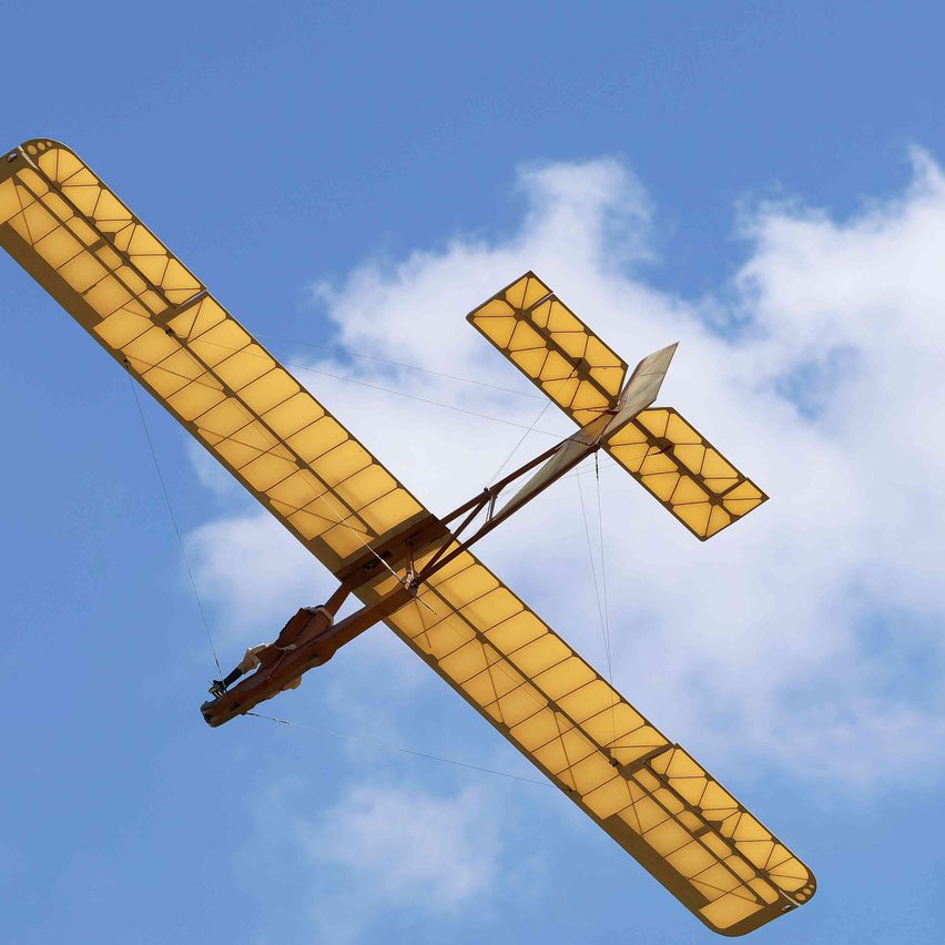 Ein Oldtimer-Doppeldeckermodell mit gelben Flügeln fliegt am blauen Himmel mit weißen Wolken.