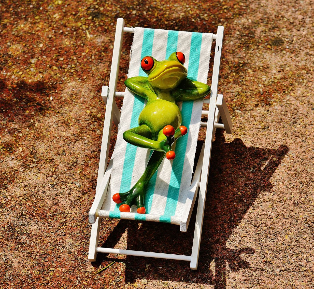 Eine grüne Froschfigur liegt auf einer weißen Liege mit blau-weißen Streifen und ruht auf der Seite.