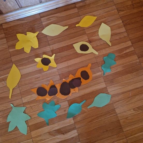 Ein Holzboden, verziert mit einer Vielzahl farbenfroher Papierblätter, einschließlich Sonnenblumen, in einem verspielten Muster angeordnet.